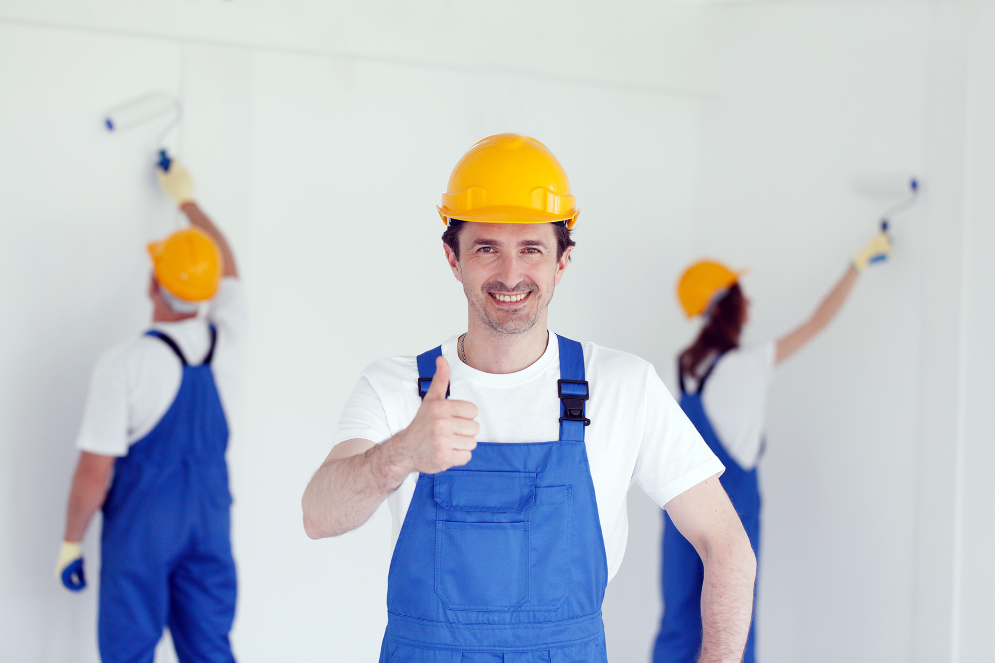 Smiling young builder in hardhat showing thumbs up indoors